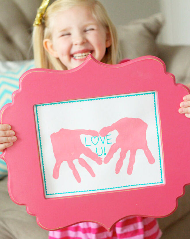 A little girl holding up a framed handprint piece for Mother's Day