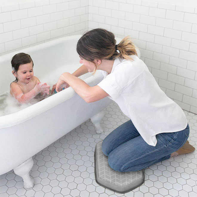 A woman bathing a baby while kneeling on a knee pad