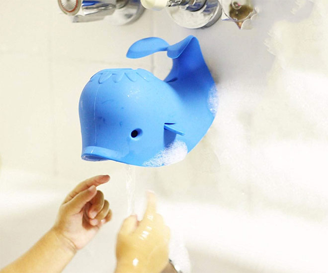 A silicone whale tap cover with water coming out of its mouth onto child's hands