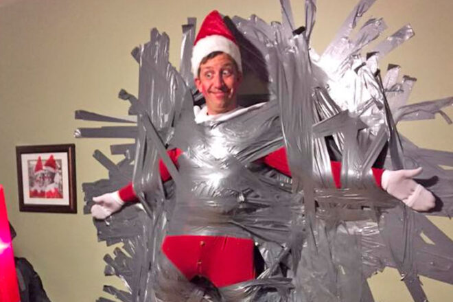 A dad dressed up as elf on the shelf duct taped to the wall