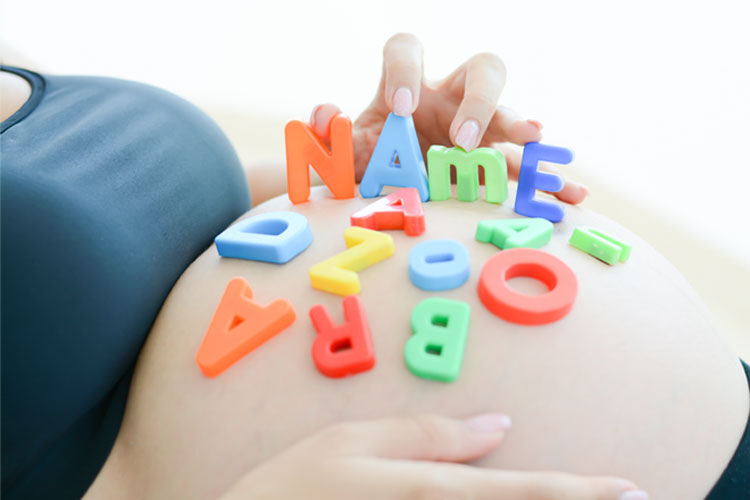 Pregnant mum with alphabet tiles on bare belly spelling out Names