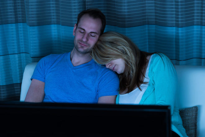 Tired couple sleeping on couch in front of TV