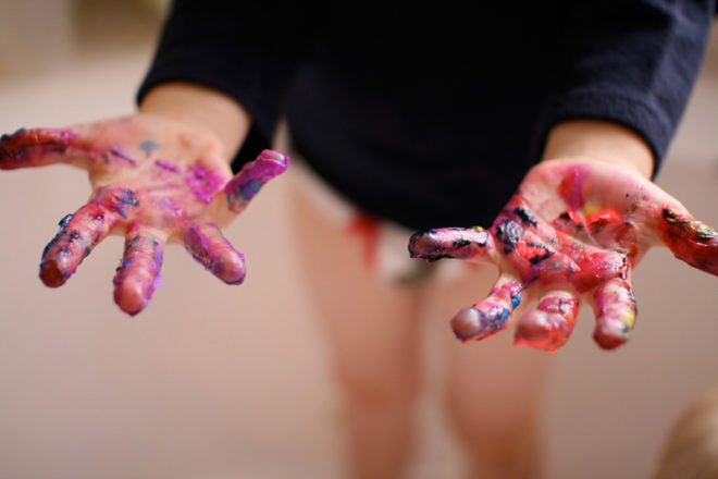 Child holding out two hands, palms up covered in paint