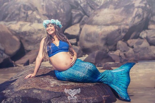 Pregnant mother dressed as mermaid on rock at beach