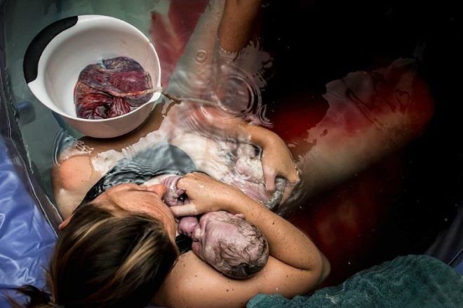 Mother holding newborn with placenta in water birth