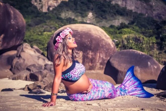 Woman holds belly on beach as a mermaid