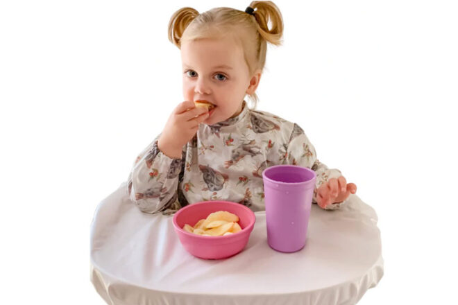 Image showing little girl wearing a Mess Me Not Smock sitting in a highchair eating food