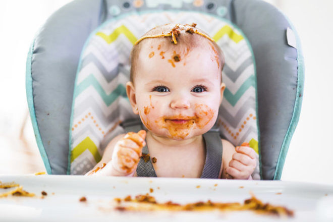 toddler in high chair eating spaghetti with hands