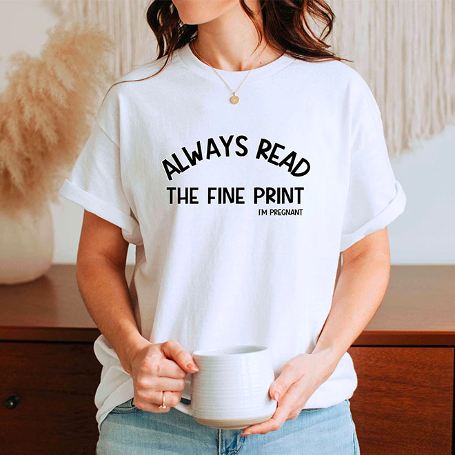 A woman wearing a white t shirt with the words 'Always Read the Fine Print - I'm pregnant' printed on the front