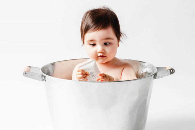 Front view of a baby sitting in a metal tub showing her holding a Gilly Goat body wash.
