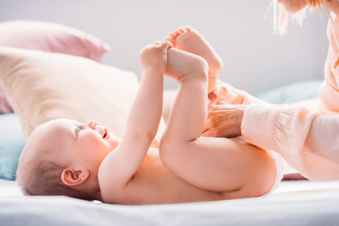 Baby laying on a bed with mum playing with him