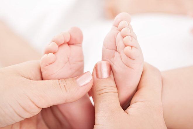 mother giving reflexology and baby massage to infants feet