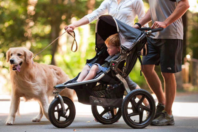 Side view of Bob Revolution Pro jogging stroller showing family on a walk with the dog, and showcasing the large all-terrain wheels on the pram.