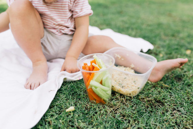 Little girl sitting on a blanket eating her lunch