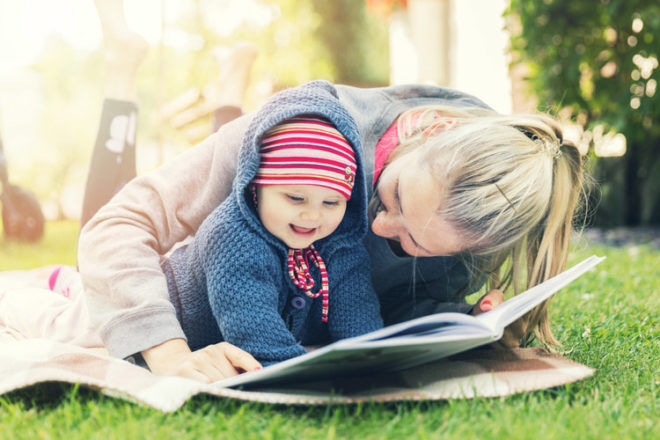 Mother and baby girl reading on a blanket outside