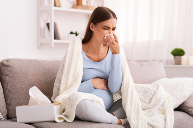 Sick Pregnant Lady Blowing Nose Sitting On Couch At Home
