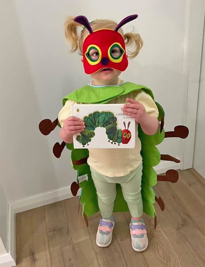 Photo showing a little girl wearing a The Very Hungry Caterpillar costume while holding up the book