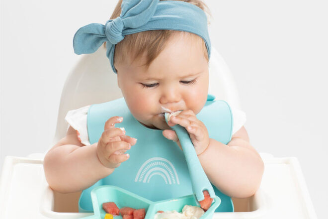 baby girl using Little Woods Silicone Baby Utensil in a high chair