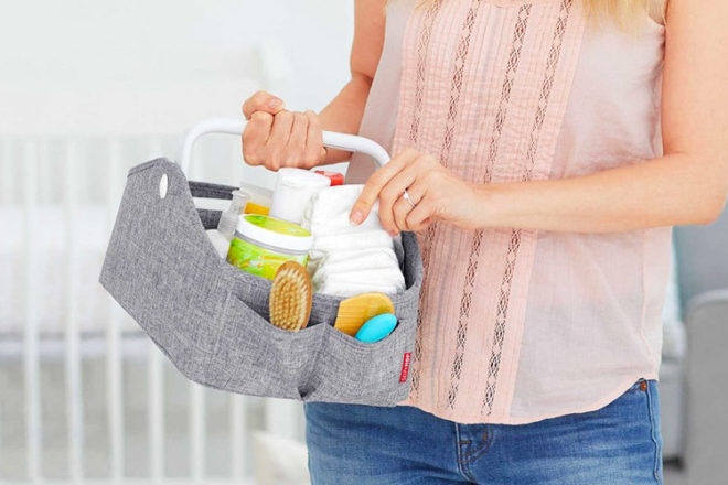 Close up of woman holding Skip Hop Diaper Organiser showing it fully stocked with changing items, and that it's portable via the sturdy carry handle .