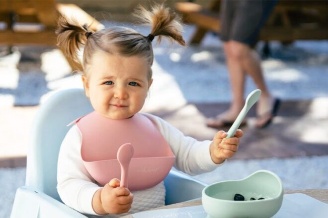 Young girl holding Wild Indiana Silicone Baby Spoons in a high chair