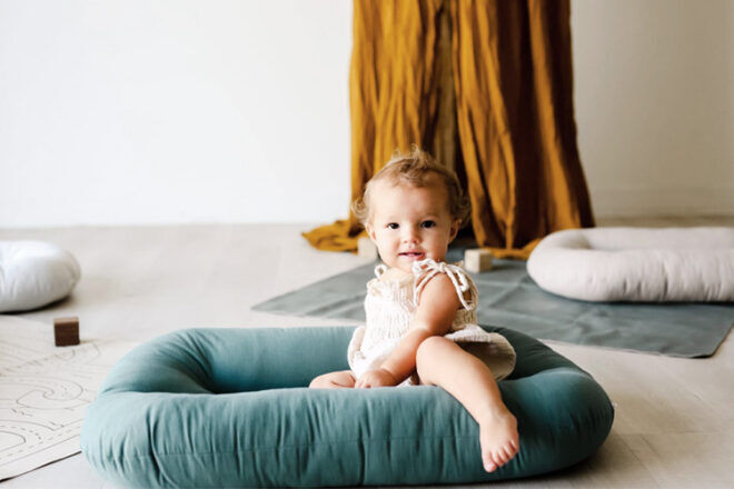 Snuggle Me Baby Lounger in Teal with a baby sitting inside the baby nest