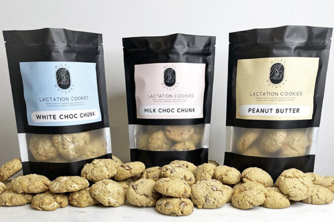 The Milky Mothers Lactation Cookies are displayed in their resealable bags, showcasing three distinct flavors: white choc chunk, milk choc chunk, and peanut butter. Loose cookies are placed in front of the bags, providing a clear view of their appearance and allowing for easy comparison of the different fillings.