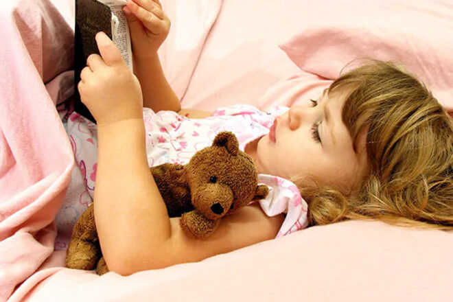 Toddler reading in bed with teddy bear 