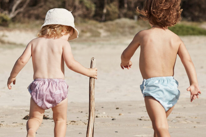 Back view of two active children wearing Econaps swim diapers, showing two different styles for comparison, Mauve Native and Ocean Native, as well as elastic legs and waistband.