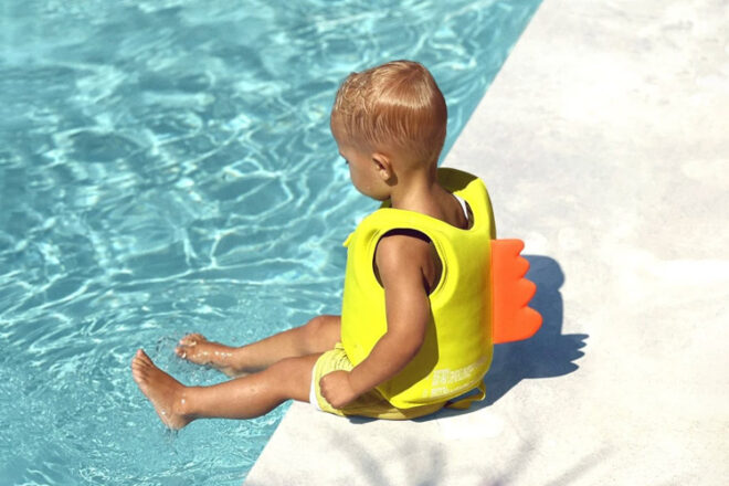 boy sitting on edge of pool wearing a sunnylife dino float jacket