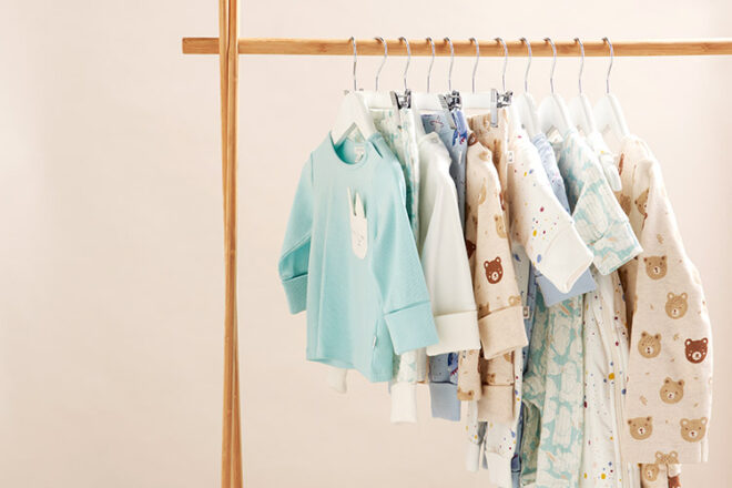 A clothing rack with Purebaby children's sleepwear items on hangers, showing the different styles, colours and prints available as well as sizes for babies through to toddlers. 