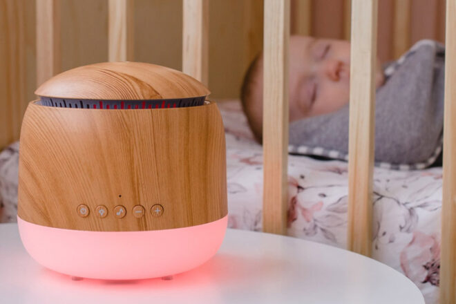 Lively Living Aroma Snooze baby humidifier sitting next to a baby cot in the nursery with the pink night light feature on