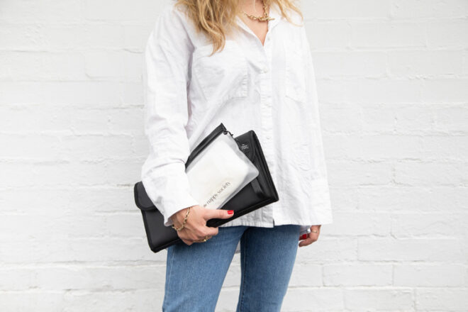 A woman is holding a Nappy Society changing clutch and wipes case, showing how both can be held with one hand.