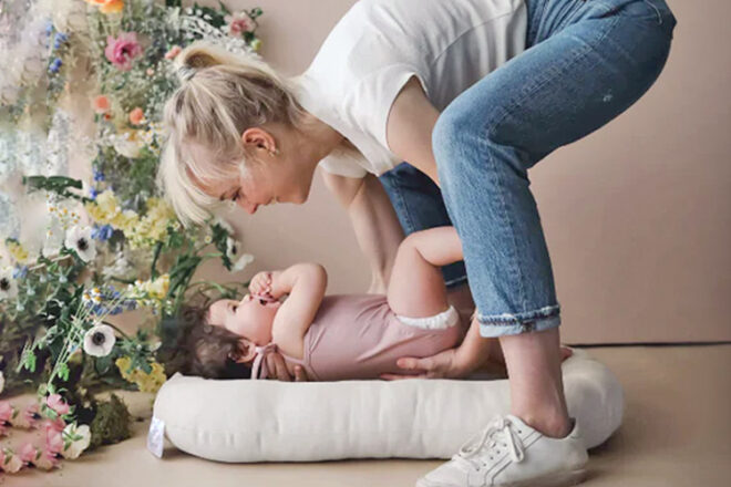 Mother placing her baby into a baby lounger on the floor. 