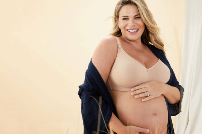 Smiling pregnant woman touching belly wearing Cake Maternity feeding bra, showing front view of smooth, wire free cups and strap.
