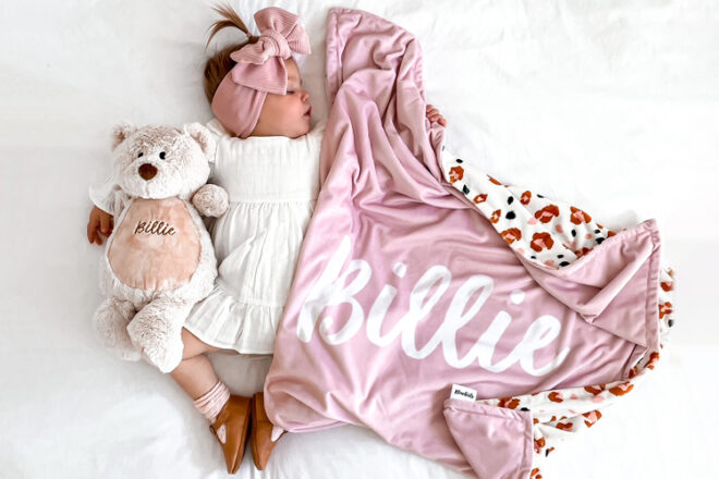 Sleeping baby girl holding a Blankid personalised baby throw, showing large name as well as reverse side with leopard print design. 