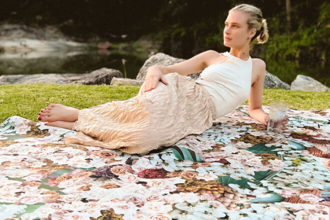 Woman lying on a murph&murph extra large picnic rug, showing the waterproof floral rose design in relaxing park setting.