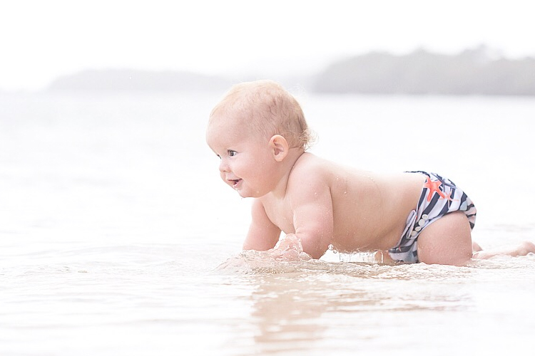 Crawling baby in ocean wearing Itti Bitti swim trunks, showing side view of use in the water as well as the nautical print.