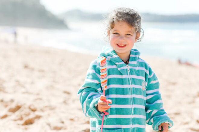 Young girl at the beach wearing Rad Kids Hooded Beach Poncho showing hood, zipper and pocket.