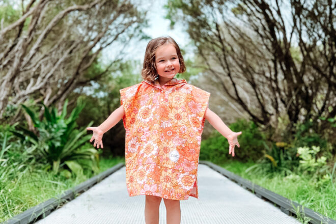 Front view of a young girl in an outdoor setting wearing Zinc & Co kids beach towel with hood, showing bright floral print.