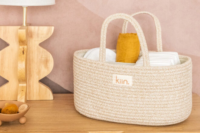 Close up of Kiin Baby baby storage basket in nursery setting, showing texture and colour of weave, carry handles and neatly stocked items inside.