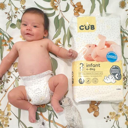 Baby wearing Coles CUB nappy lying on bed