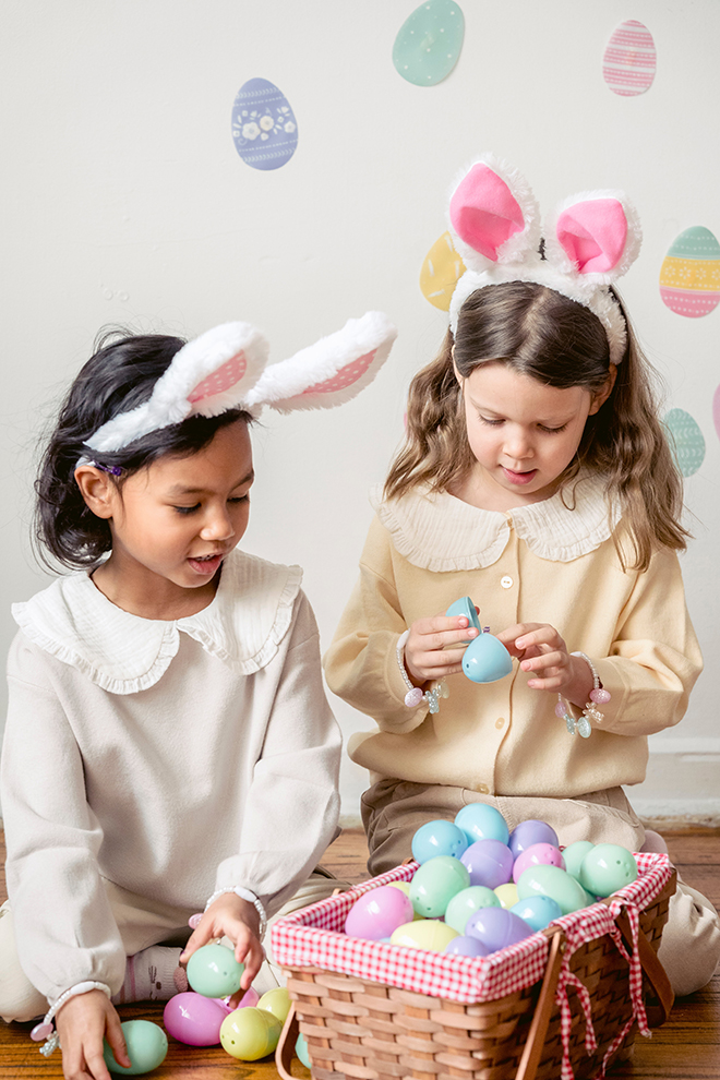 Two girls with bunny ears on looking inside an Easter basket full of eggs