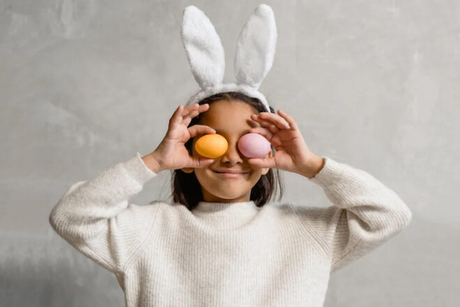 Girl with bunny ears hold two Easter eggs to her eyes