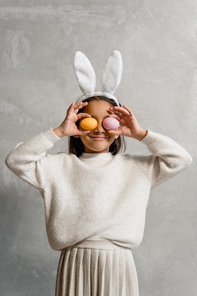 Girl with bunny ears hold two Easter eggs to her eyes