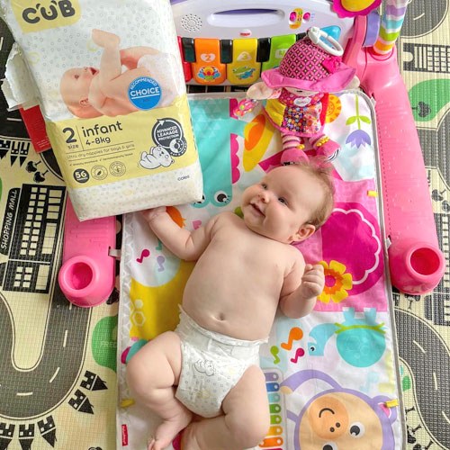 Baby wearing Coles CUB nappy lying on play mat