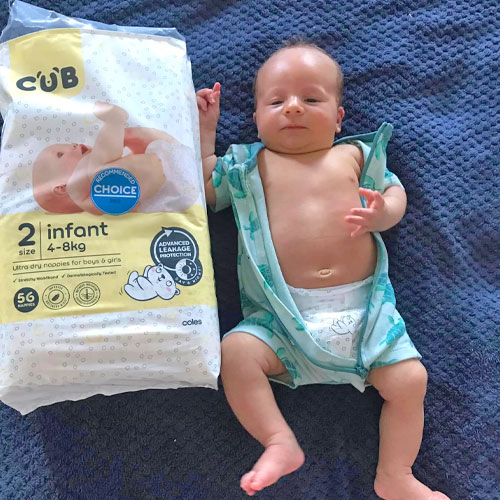 Baby wearing Coles CUB nappy lying on bed