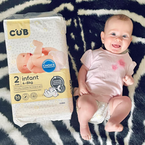 Baby wearing Coles CUB nappy lying on rug