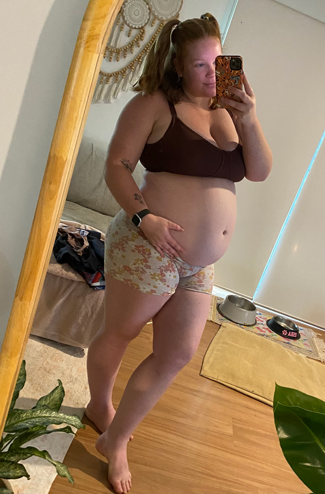 Brittany pregnant at 25 weeks looking in the mirror with bare belly bump