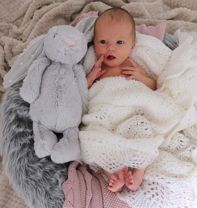 A baby wrapped up in a blanket next to a soft toy.