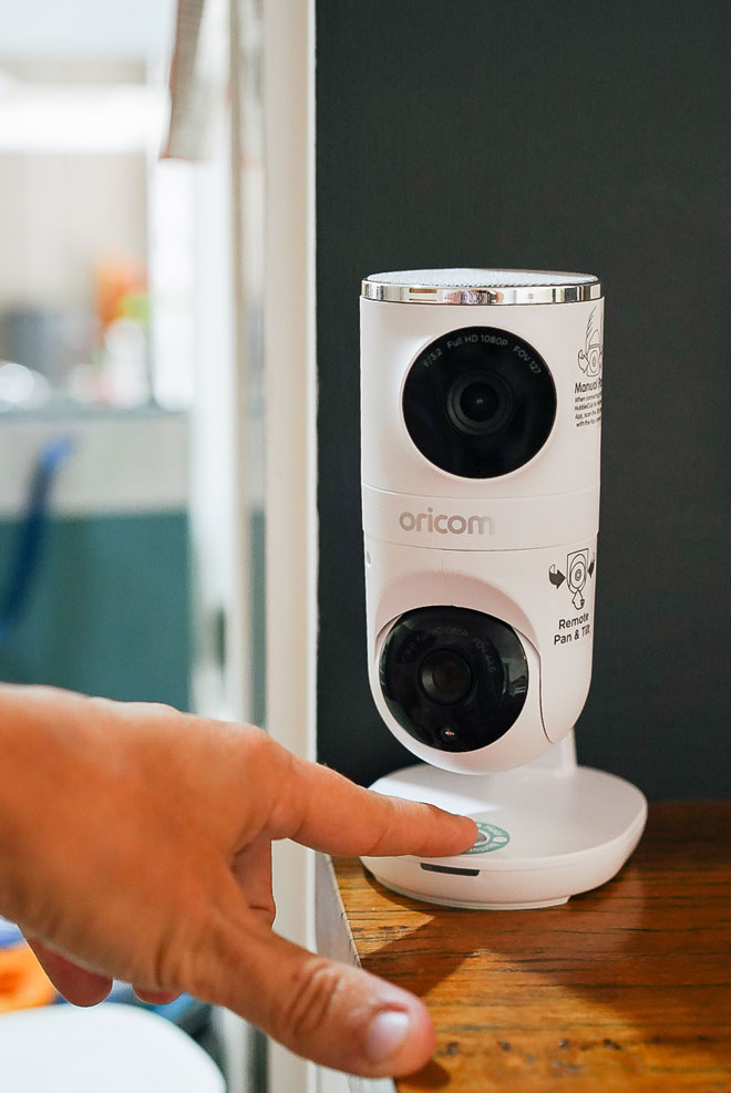 Oricom Dual Camera Baby Monitor with a ladies finger pressing the talk button